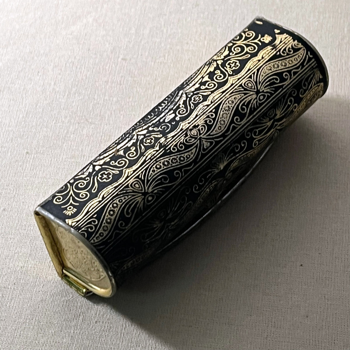 Estuche de pintalabios negro y dorado, vista de tres cuartos con la bisagra