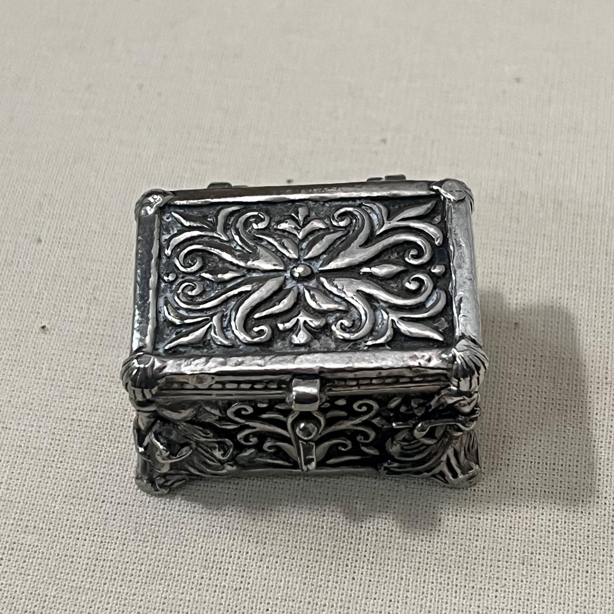 Cofre joyero en miniatura de metal plateado con relieve de volutas, cerrado, 3 cm