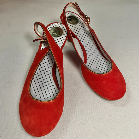Par de zapatos destalonados en ante rojo con tacón de carrete, tira de talón con hebilla dorada y plantilla blanca de lunares negros, vistos de tres cuartos.