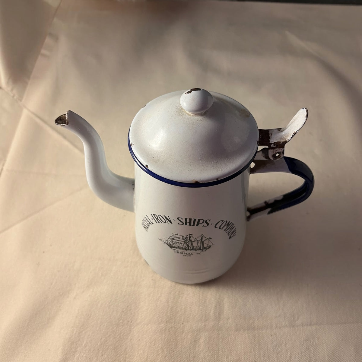 Cafetera esmaltada blanca con ribete azul y velero impreso, tapa abatible, vista lateral