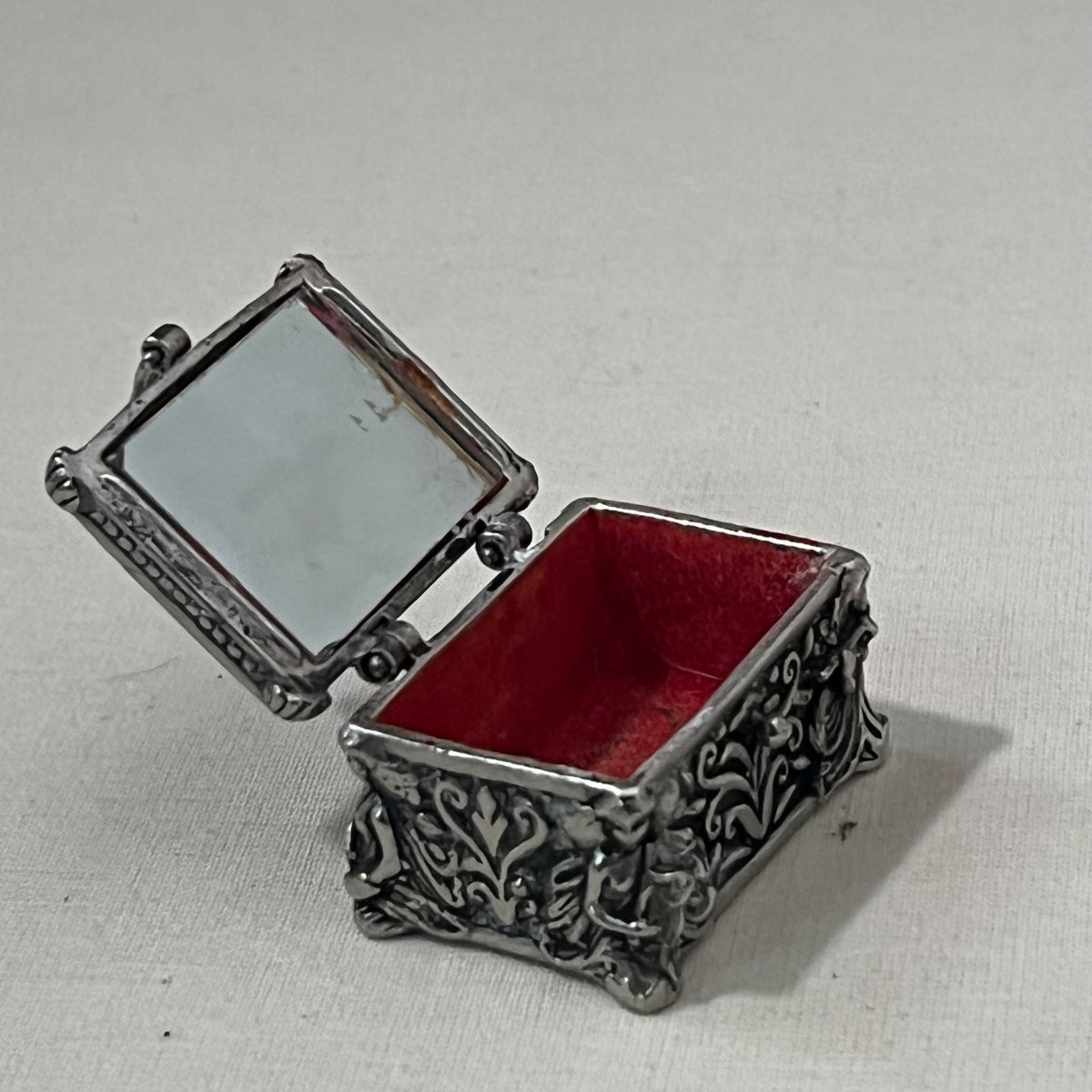 Cofre joyero en miniatura abierto, con espejo en la tapa e interior de terciopelo rojo