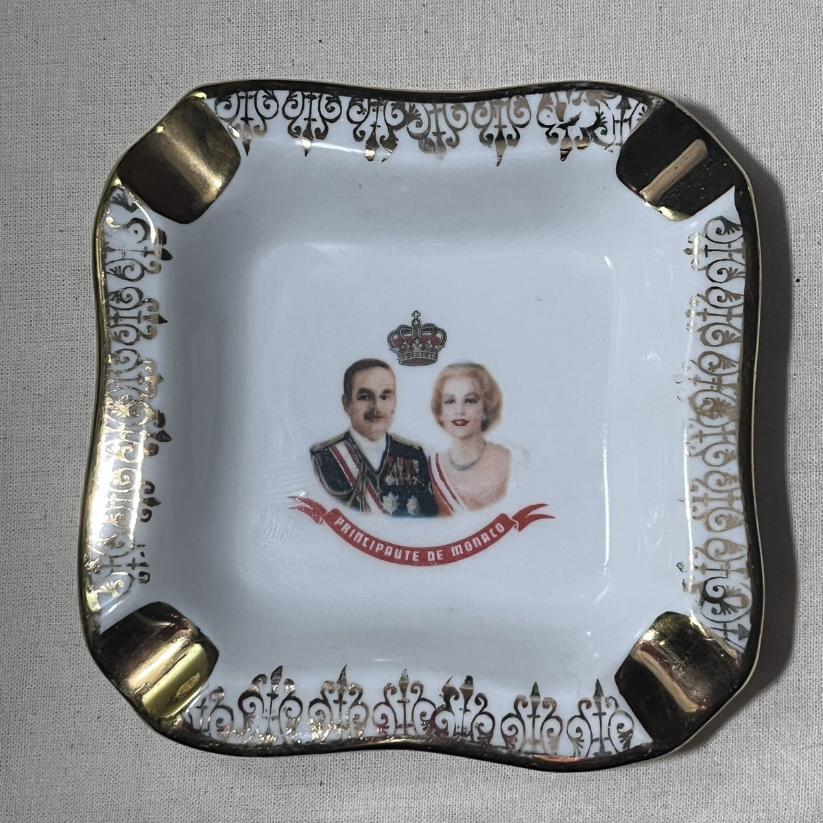 Cenicero cuadrado de porcelana de Limoges con retratos de Rainiero III y Grace de Mónaco bajo corona, ala con volutas doradas