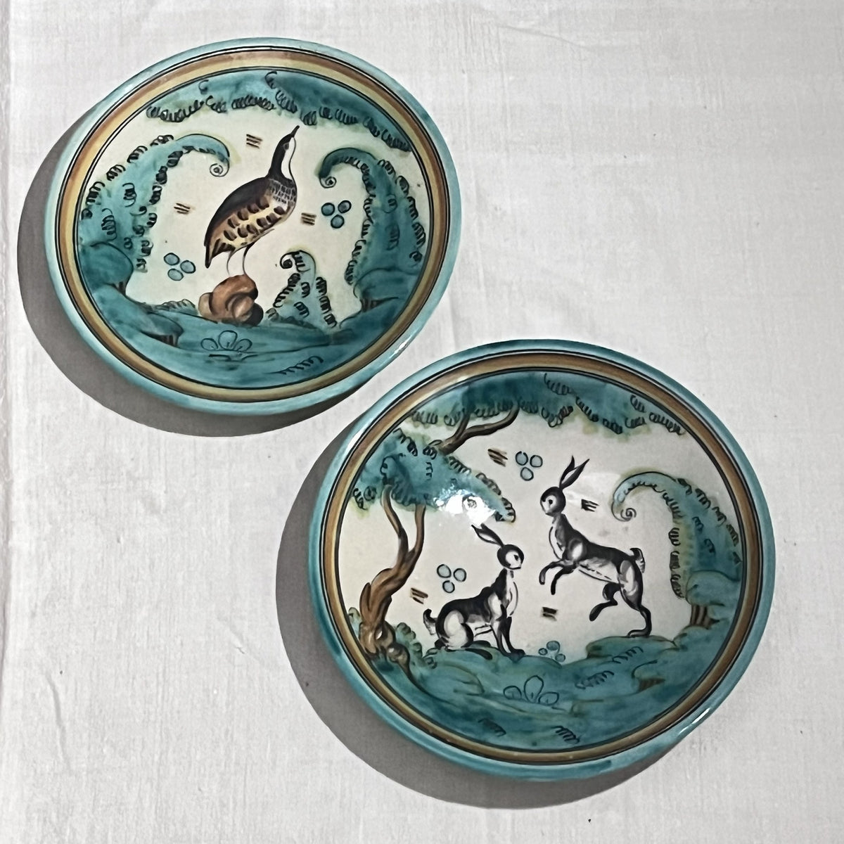 Pareja de platos de cerámica pintados a mano con liebres y una perdiz en tonos verdes, vista frontal